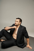handsome man with bristle posing in pinstripe suit while adjusting sleeve on jacket on grey backdrop t-shirt #692776516