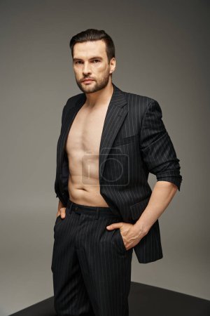 bel homme brune dans la trentaine posant avec les mains dans des poches en costume de pinstripe sur fond gris