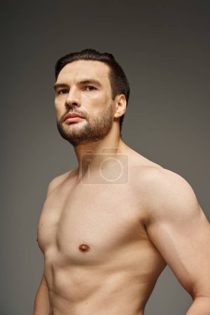 retrato de hombre sin camisa y guapo con cerdas y pecho desnudo posando sobre fondo gris