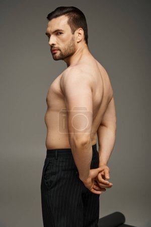 portrait of shirtless handsome man with bristle and bare chest posing in pants on grey background