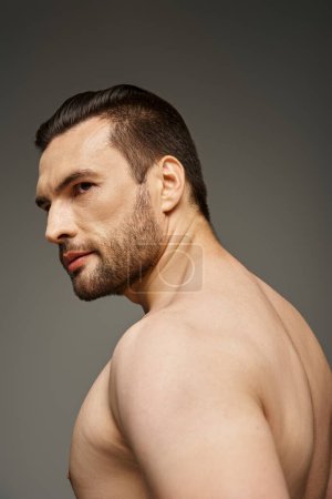 retrato de hombre sin camisa y guapo con cerdas mirando hacia otro lado mientras posando sobre fondo gris
