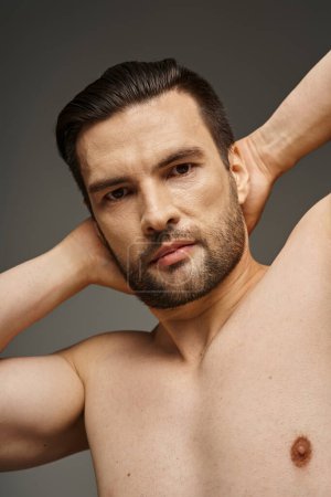 Porträt eines muskulösen und hemdlosen Mannes mit nackter Brust und Borsten, der vor grauem Hintergrund posiert