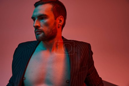 Téléchargez les photos : Portrait d'homme à poitrine nue posant en costume de pinstripe élégant en studio avec lumière rouge et bleue - en image libre de droit