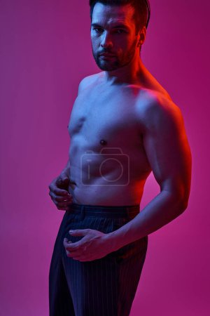 Téléchargez les photos : Portrait d'un bel homme posant en pantalon à rayures sur fond violet avec des lumières rouges et bleues - en image libre de droit