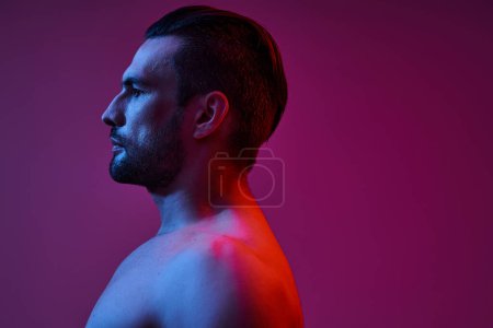 Téléchargez les photos : Vue latérale de l'homme séduisant et musclé avec soies posant sur fond violet, prise de vue de mode - en image libre de droit