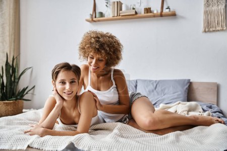 Téléchargez les photos : Heureuse femme afro-américaine regardant petite amie tout en étant couché ensemble sur le lit, l'intimité et l'amour - en image libre de droit