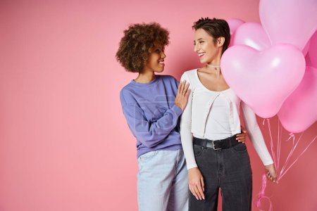 Valentinstag-Konzept, glückliches multikulturelles lesbisches Paar lächelt in der Nähe herzförmiger Luftballons