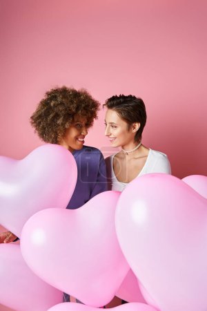 Concept de Saint Valentin, heureux couple lesbien interracial souriant près de ballons roses en forme de coeur