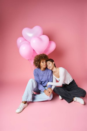 young multicultural lesbian couple sitting near pink heart shaped balloons, Saint Valentines day