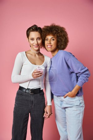 cheerful lesbian woman holding present and hand of african american girlfriend on Valentins day