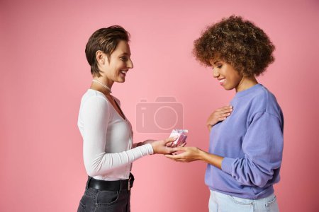 cheerful lesbian woman giving present to joyful african american girlfriend on Valentins day