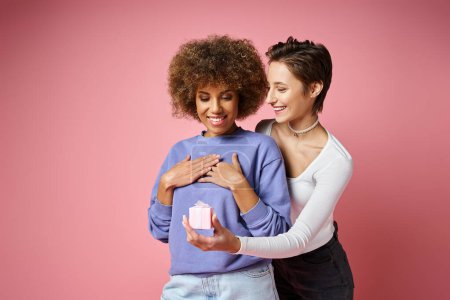 cheerful lesbian woman giving present to amazed african american girlfriend on Valentins day