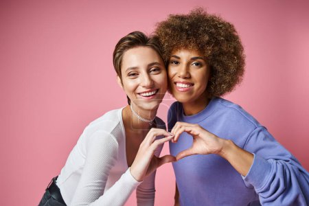 glückliches multikulturelles lgbtq Paar zeigt Herzzeichen mit Händen auf rosa Hintergrund, Liebe