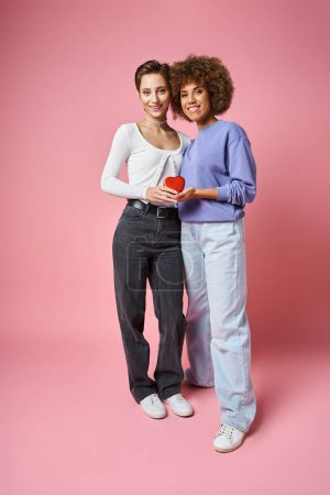 heureux couple multiculturel lgbtq tenant boîte en forme de coeur rouge sur fond rose, Saint Valentin