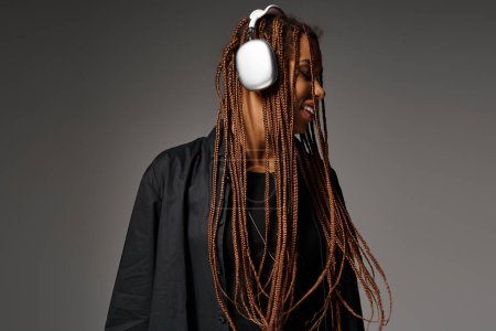 lebensfrohe junge Afroamerikanerin in den 20er Jahren mit Kopfhörern, die vor grauem Hintergrund Musik hört