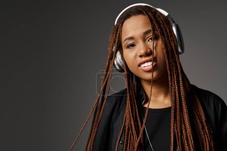 portrait of happy african american young woman in dreadlocks listening music in headphones on grey