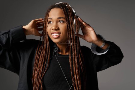 portrait of dreamy african american girl with dreadlocks listening music in headphones on grey