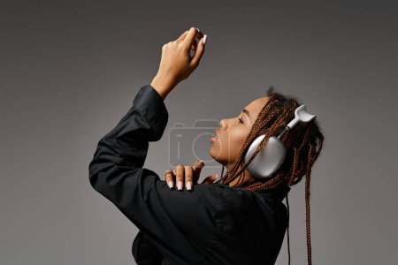 Photo for African american woman with dreadlocks listening music in headphones and looking away on grey - Royalty Free Image