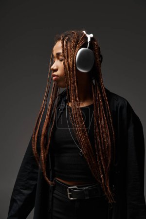 african american girl with dreadlocks listening music in headphones on grey background, closed eyes