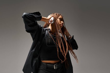 ecstatic dance of african american woman in her 20s with dreadlocks and wireless headphones on grey