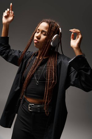 danse extatique de la jeune femme afro-américaine avec dreadlocks et écouteurs sans fil sur gris