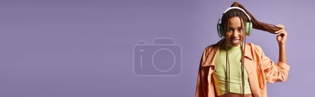happy african american young woman in headphones holding her dreadlocks on purple background, banner