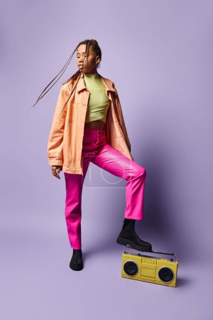 stylish african american girl with dreadlocks stepping on retro boombox on purple backdrop