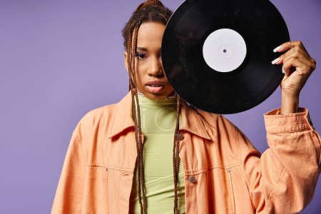 african american woman in her 20s with dreadlocks covering half of face with vinyl disc on purple
