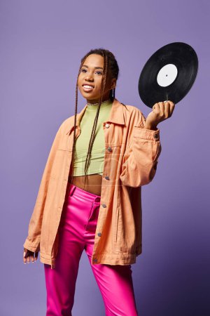 happy young african american girl in her 20s with dreadlocks holding vinyl disc on purple backdrop