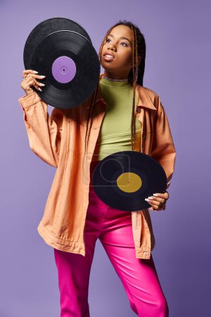 nachdenkliches afrikanisch-amerikanisches Mädchen in ihren Zwanzigern mit Dreadlocks, die Schallplatten auf lila Hintergrund halten