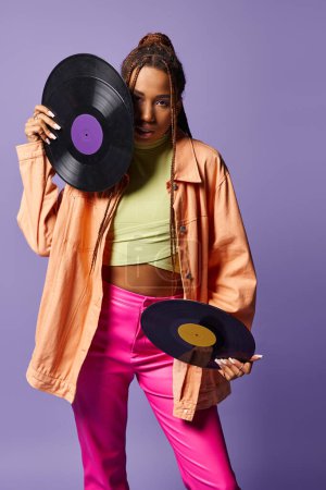 young african american girl in her 20s with dreadlocks holding vinyl discs on purple backdrop