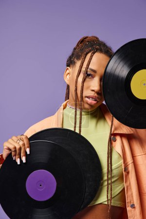 joven afroamericana chica en su 20s con rastas posando con discos de vinilo sobre fondo púrpura