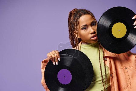 young african american woman in her 20s with dreadlocks posing with vinyl discs on purple backdrop