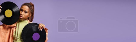 Téléchargez les photos : Afro-américaine fille dans sa vingtaine avec dreadlocks posant avec des disques de vinyle sur fond violet, bannière - en image libre de droit