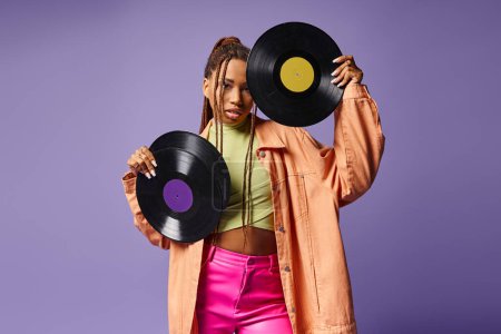 Photo for Stylish african american woman in her 20s with dreadlocks posing with vinyl discs on purple backdrop - Royalty Free Image