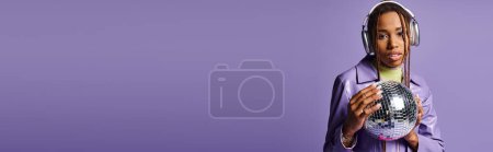 Téléchargez les photos : Jeune fille afro-américaine dans des écouteurs sans fil élégants tenant boule disco sur violet, bannière - en image libre de droit