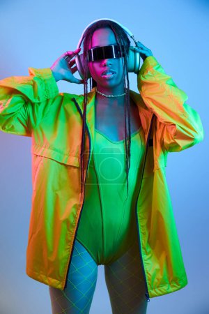 young african american woman in wireless headphones and bodysuit standing in studio with neon lights