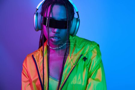 hübsche Afroamerikanerin mit Kopfhörern und stylischer Sonnenbrille posiert im Studio mit Neonlicht