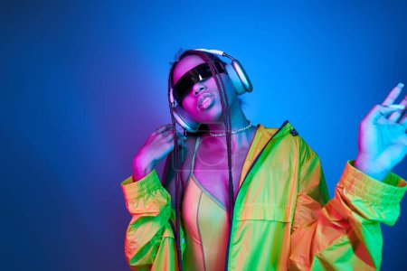 african american girl in headphones and stylish sunglasses listening music in studio with lights