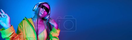 Photo for African american girl in headphones and sunglasses listening music in studio with lights, banner - Royalty Free Image