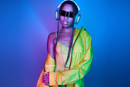 beautiful dark-skinned girl in headphones posing in bodysuit and jacket in studio with neon lights