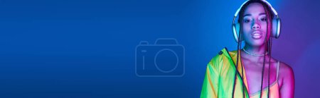 Téléchargez les photos : Bannière horizontale de belle femme à la peau foncée dans les écouteurs posant en studio avec des néons - en image libre de droit