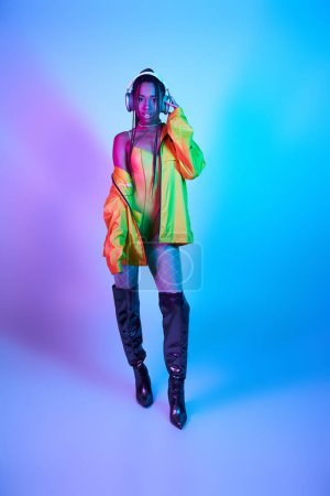 dark-skinned girl in headphones posing in bodysuit and over knee boots in studio with neon lights
