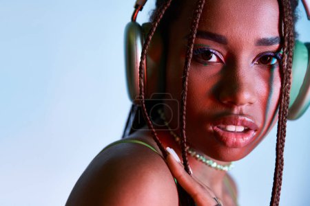 Foto de Mujer afroamericana joven con rastas en auriculares inalámbricos mirando a la cámara en azul - Imagen libre de derechos