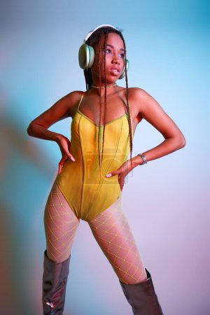 junge Afroamerikanerin mit Kopfhörern posiert in gelbem Body und Overknee-Stiefeln im Studio