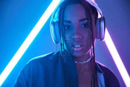 Foto de Retrato de chica afroamericana en rastas y auriculares en estudio con luz fluorescente azul - Imagen libre de derechos