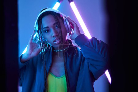beautiful african american girl in headphones enjoying music in studio with fluorescent light