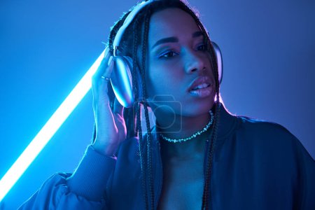 Photo for Beautiful african american woman in headphones enjoying music in studio with fluorescent light - Royalty Free Image