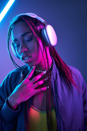 Photo for African american woman in headphones enjoying music in studio with fluorescent light, ecstatic - Royalty Free Image