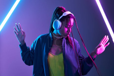 Photo for African american woman in headphones enjoying music in studio with fluorescent light, dance - Royalty Free Image